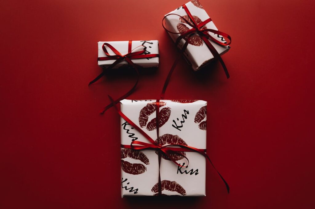 Stylish gift boxes wrapped with lip-print paper and red ribbons on a red background.